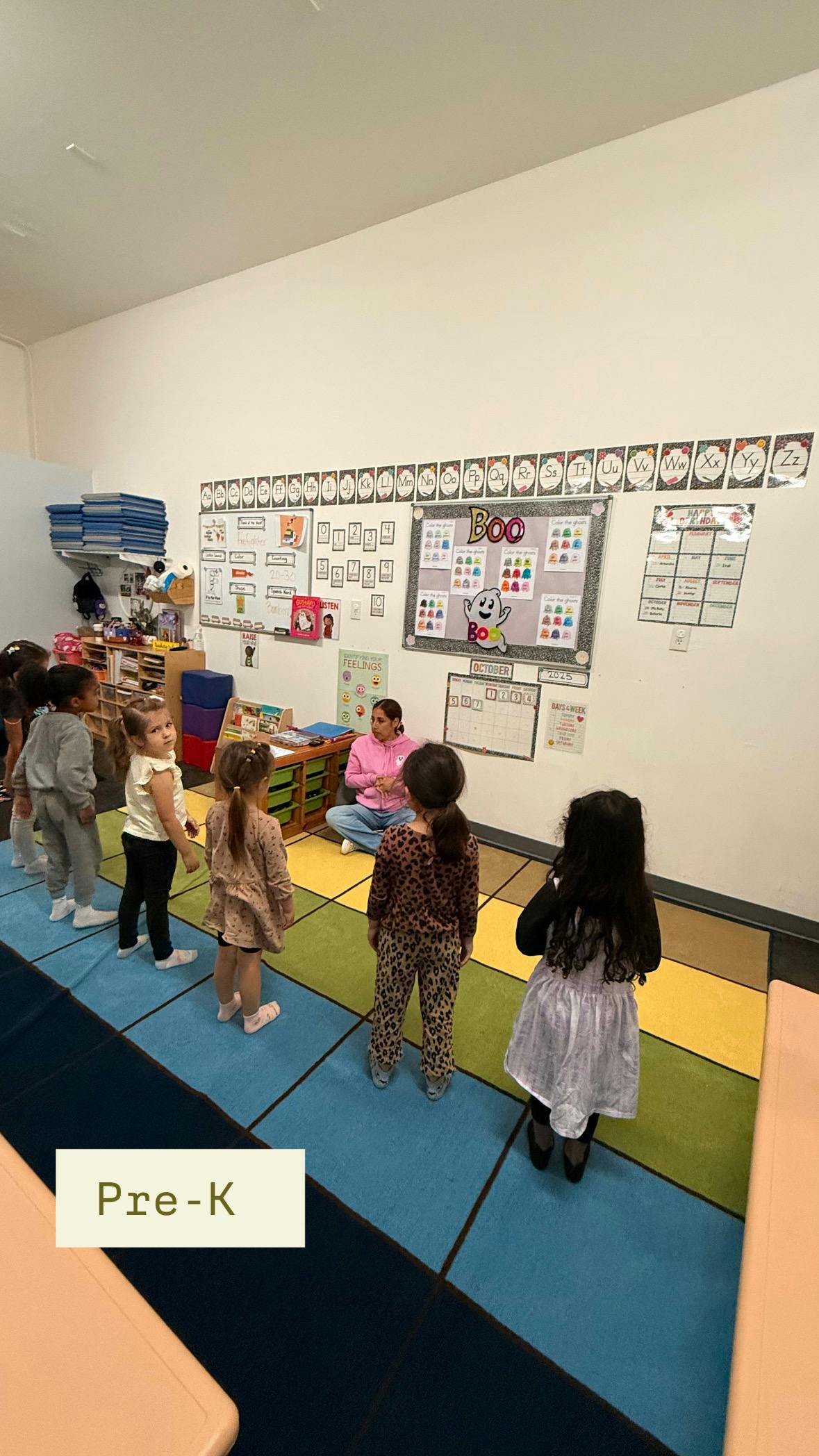 Adult sitting on floor with children standing in classroom