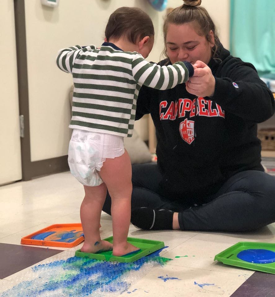 Person helping a child stand on a green tray with blue paint