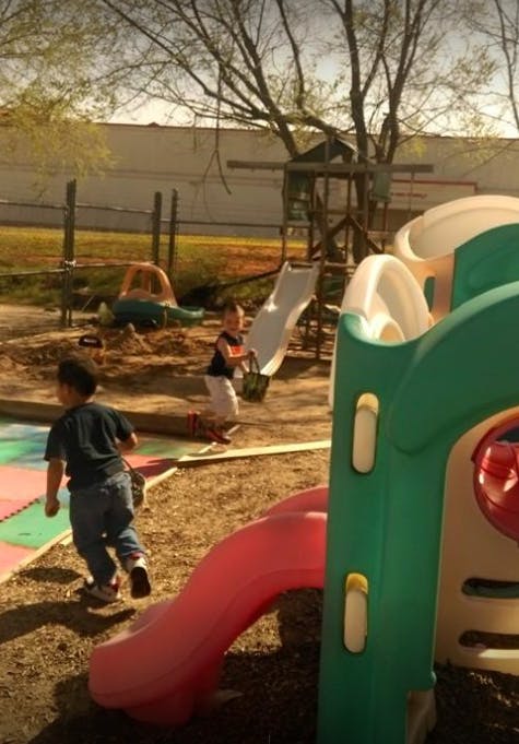 Two children playing on a playground with slides and a wooden structure