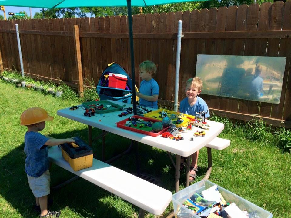 Three children playing with toys at a picnic table outdoors