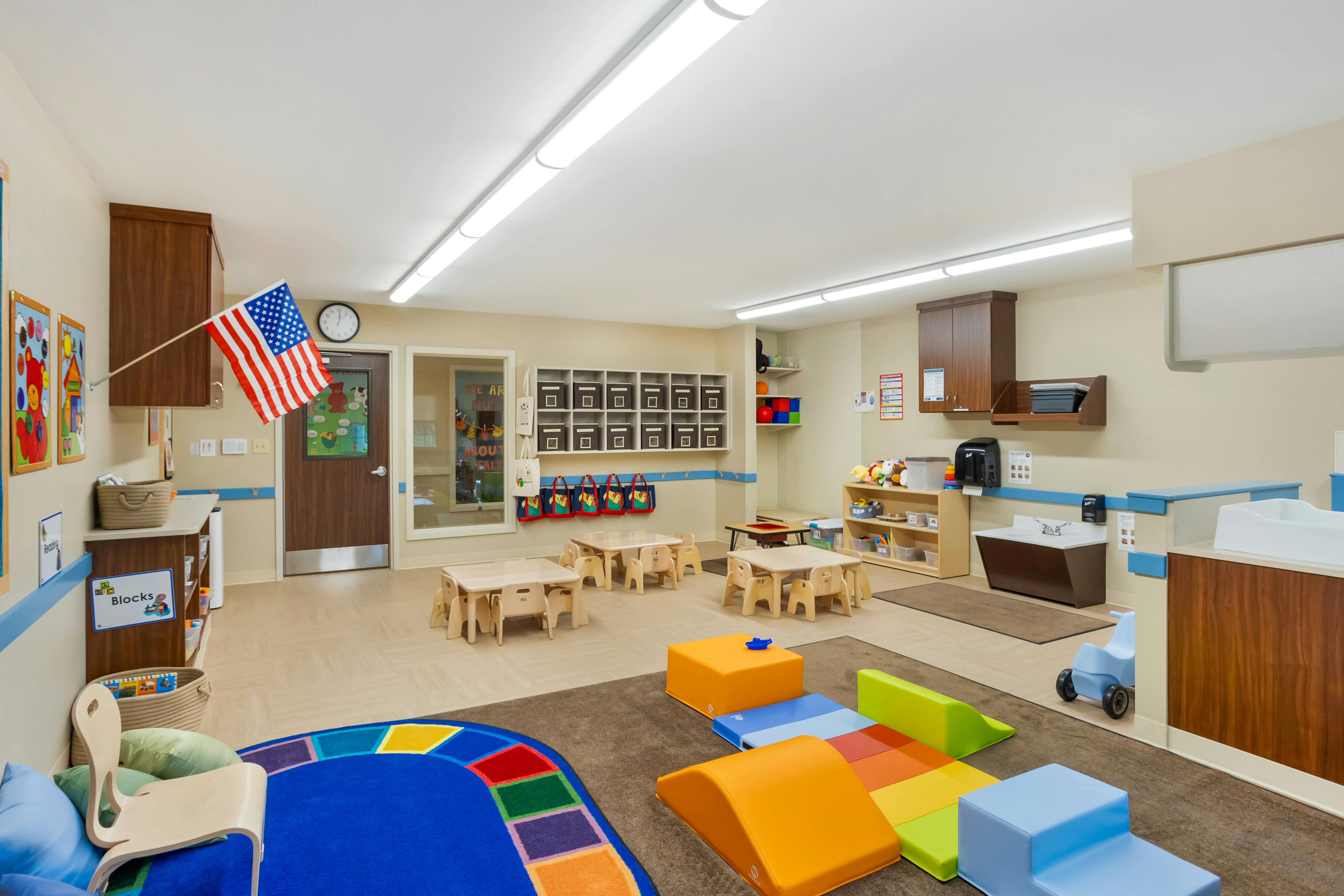 Children's playroom with small tables, chairs, play equipment, and an American flag