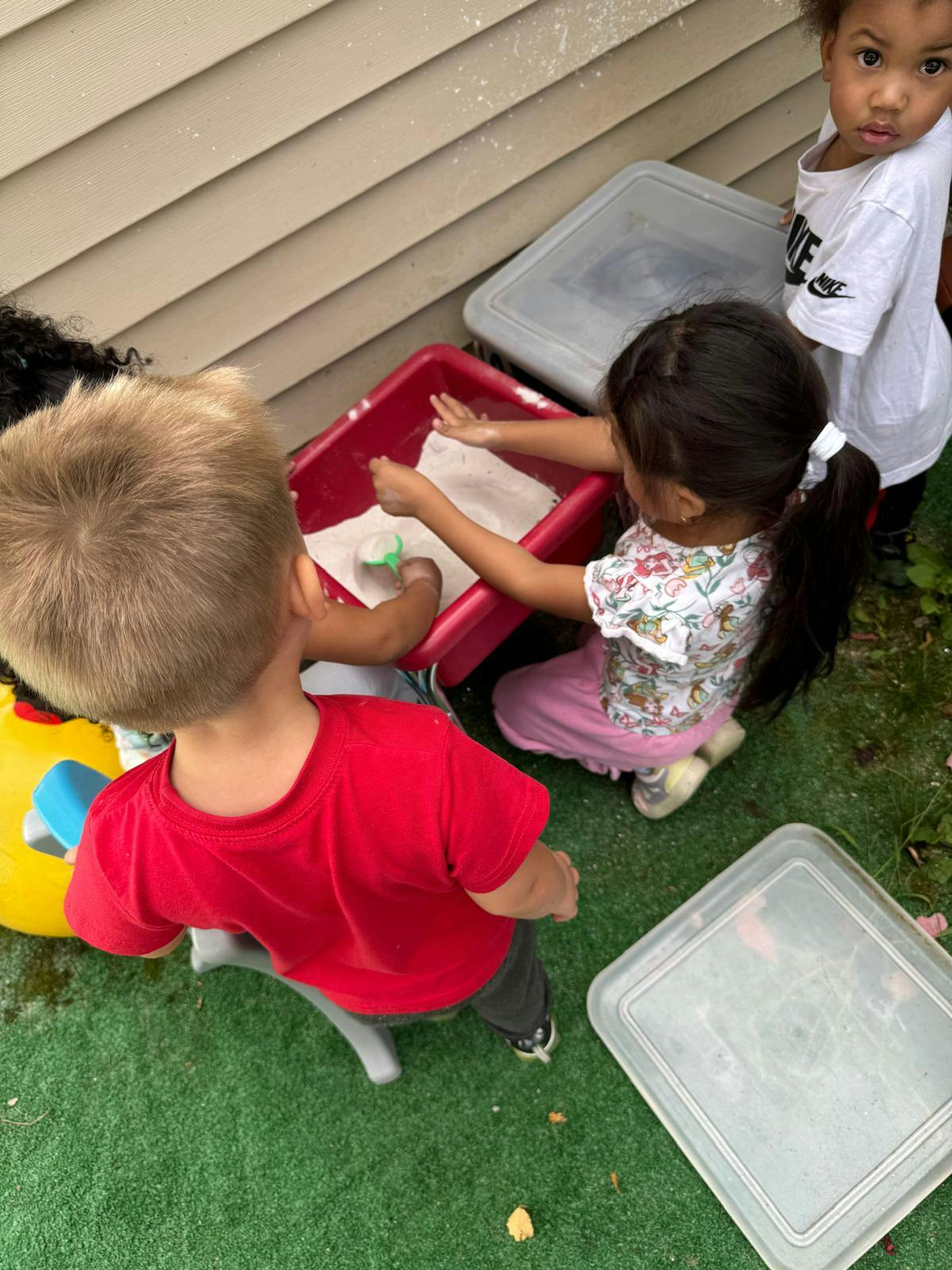 Children playing with sand in a red tray outdoors