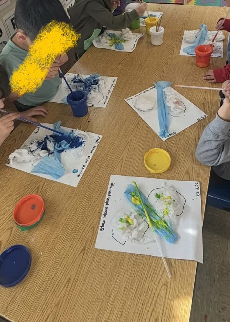 Children using straws to create art on paper at a table