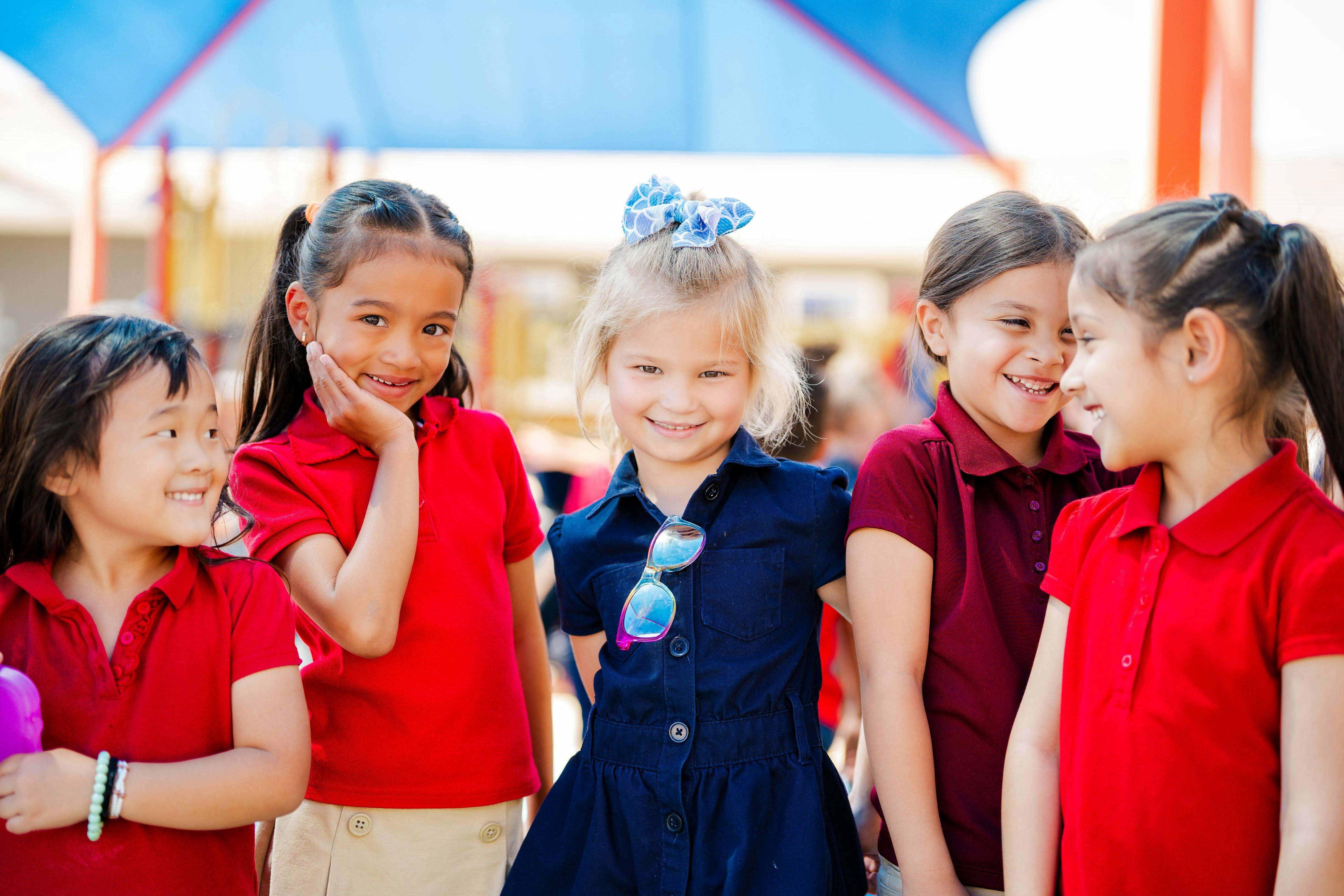 Five children standing together, three in red shirts and two in blue dresses