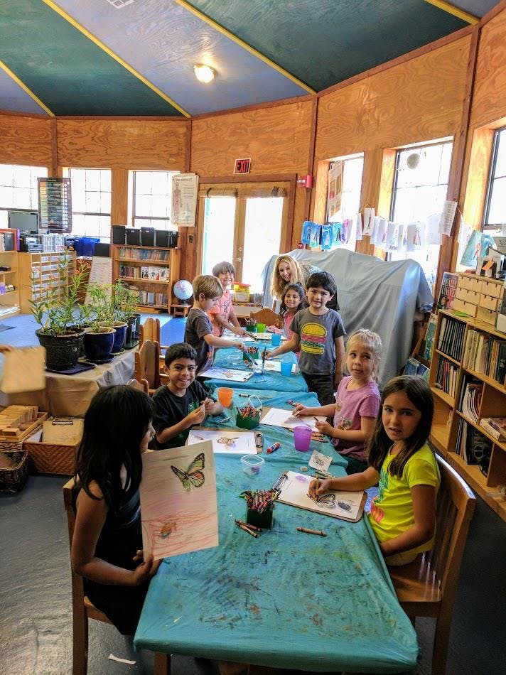 Children sitting at tables in a classroom, drawing and coloring