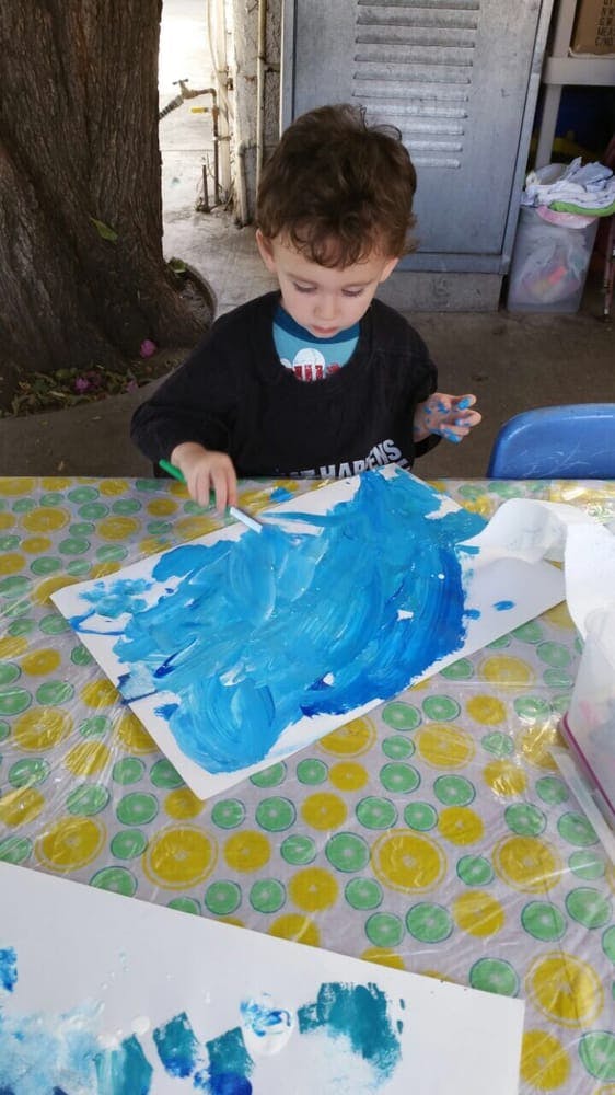 Child painting with blue paint on a canvas