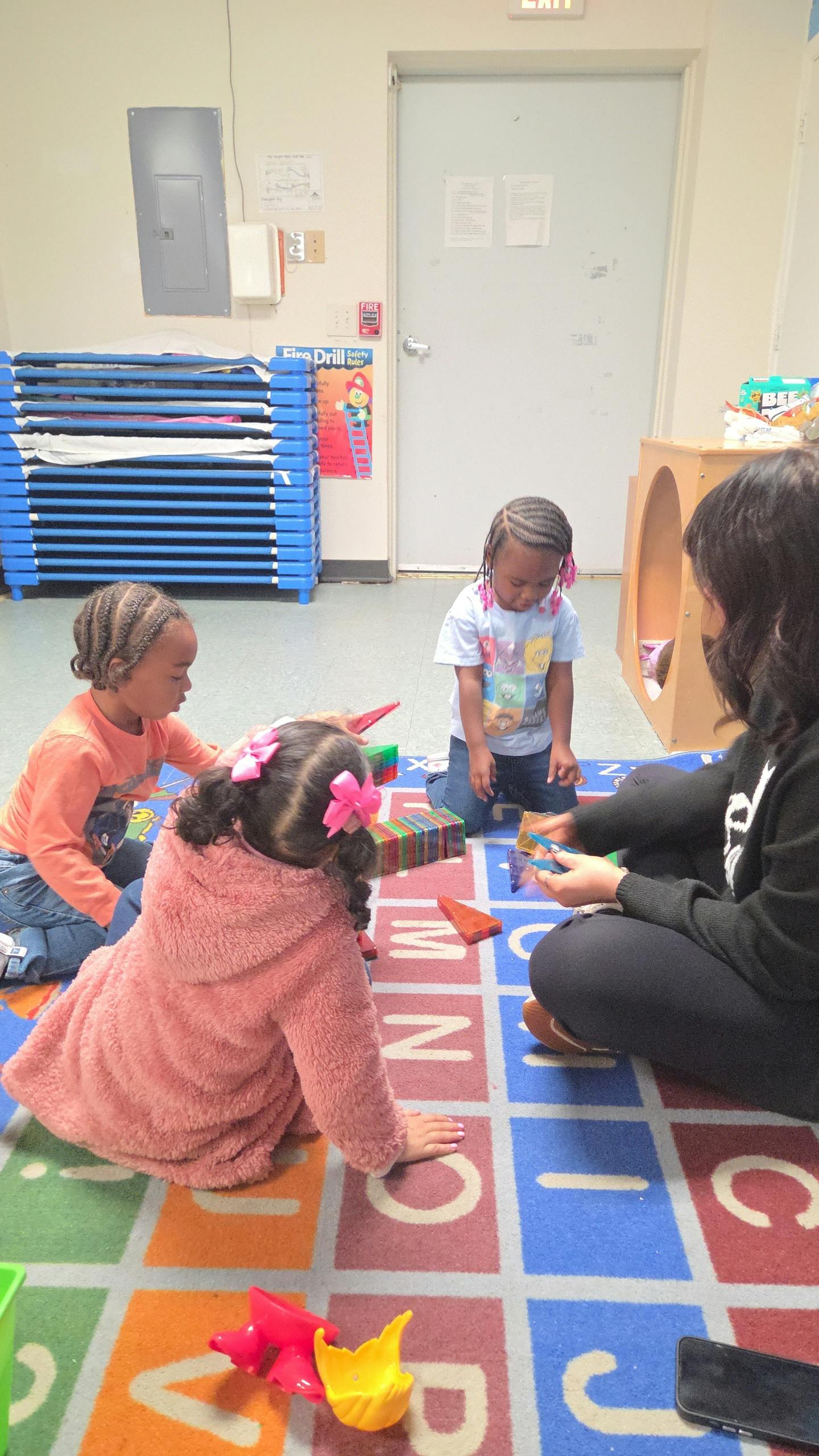 Three children and an adult on a patterned floor, playing with colorful blocks