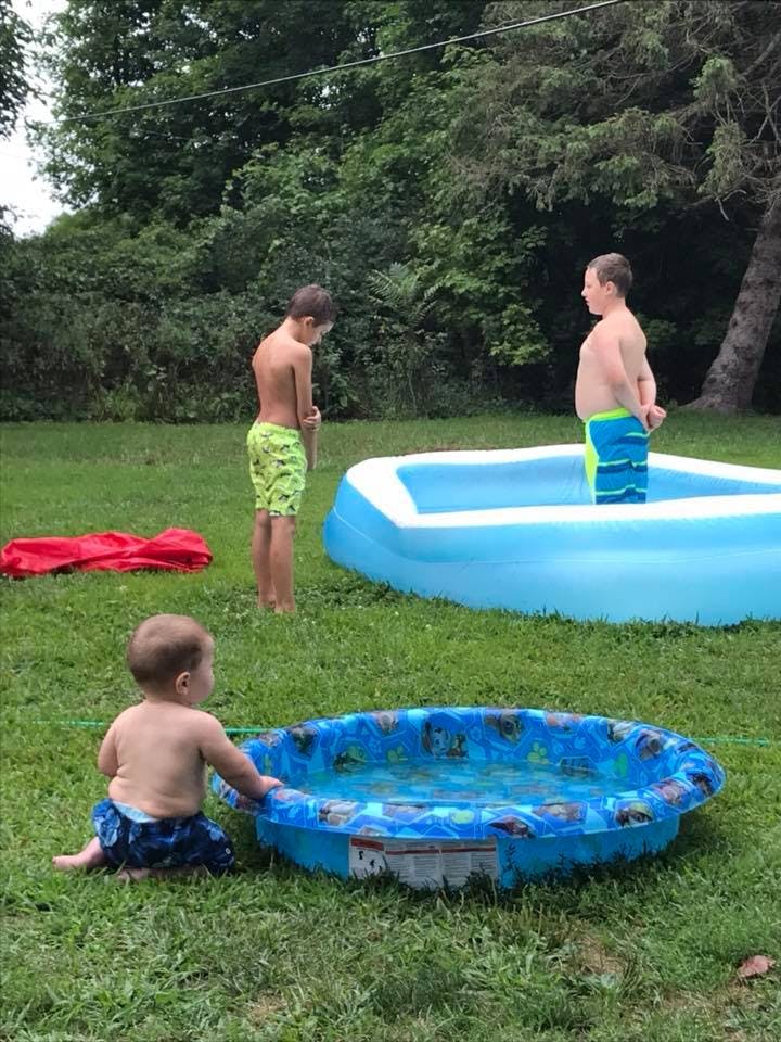 Three children with two inflatable pools in a grassy yard
