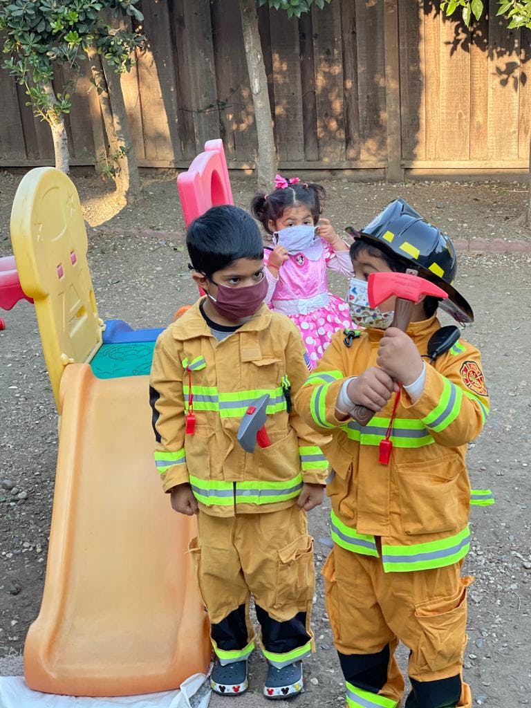 Two children in firefighter costumes and one child in a pink dress