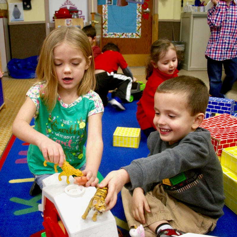 Two children playing with toy animals in a classroom