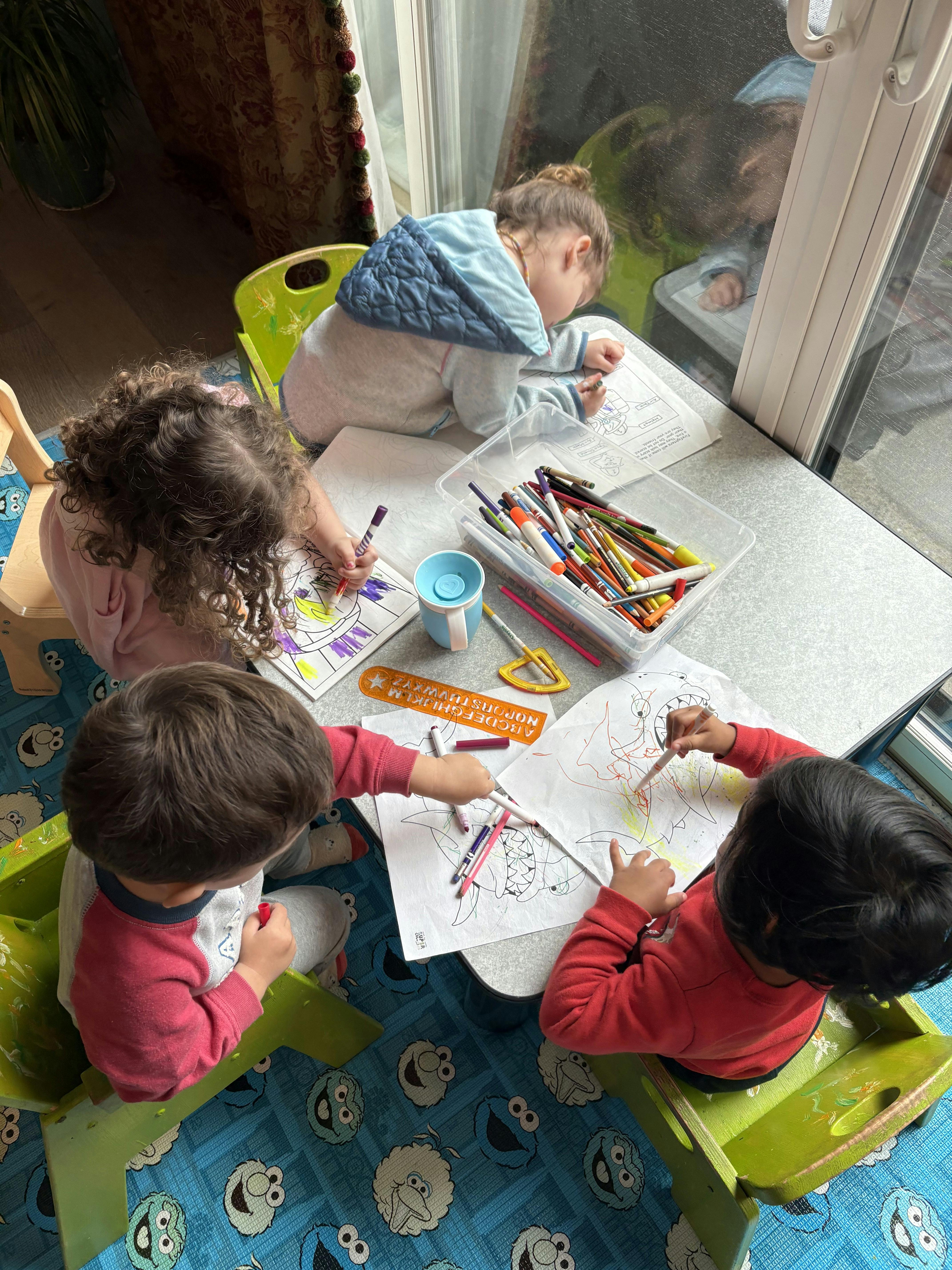 Three children drawing and coloring at a table with markers and markers