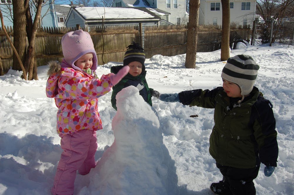 Three children building a snowman in the snow