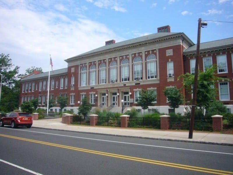 Red brick building with white trim and many windows next to a street
