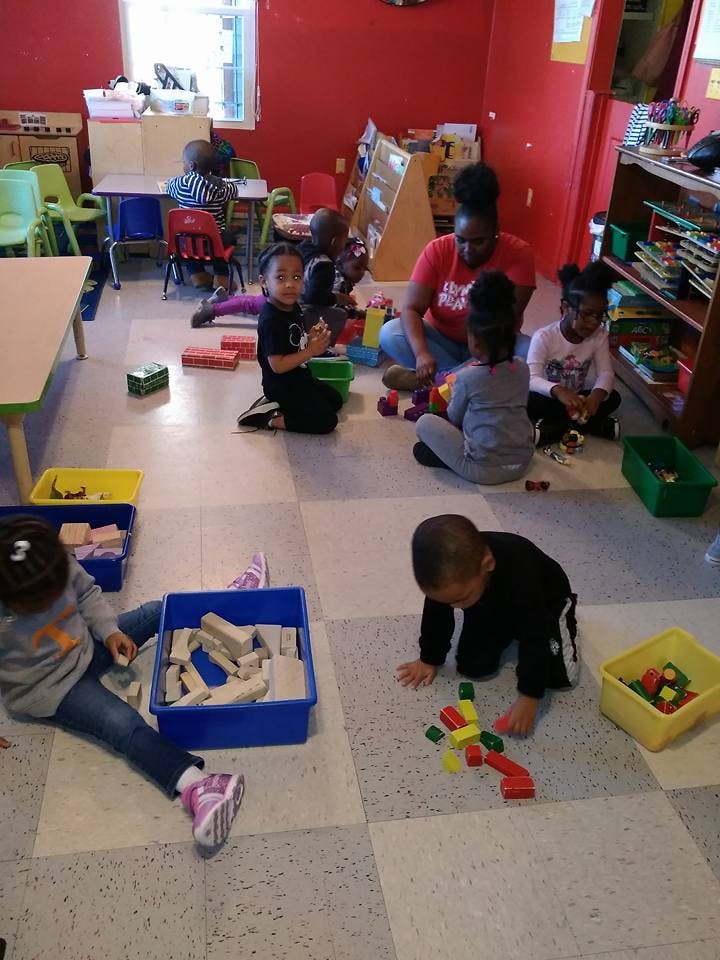 Adult and children playing with blocks on the floor in a classroom