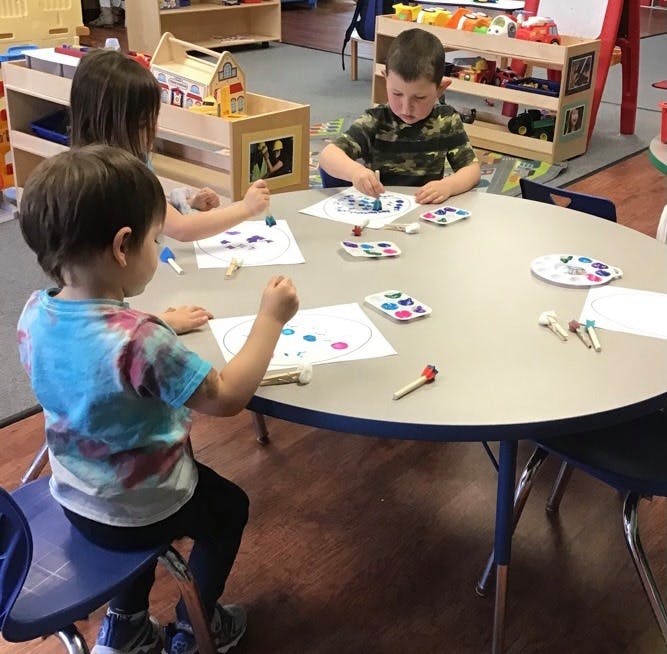 Three children sitting at a table doing an art activity