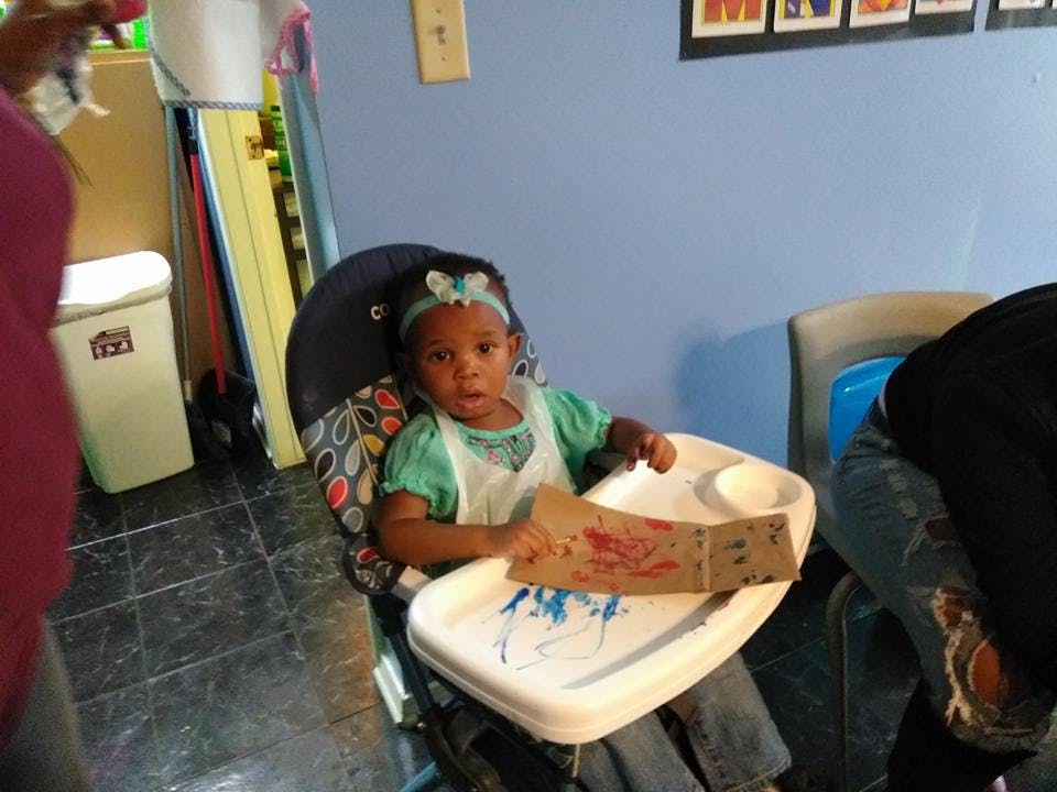 Child in a high chair with a bib and a piece of paper with markings