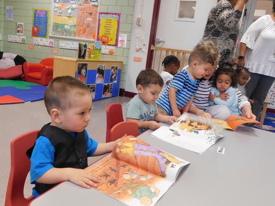 Children sitting at a table looking at books in a classroom