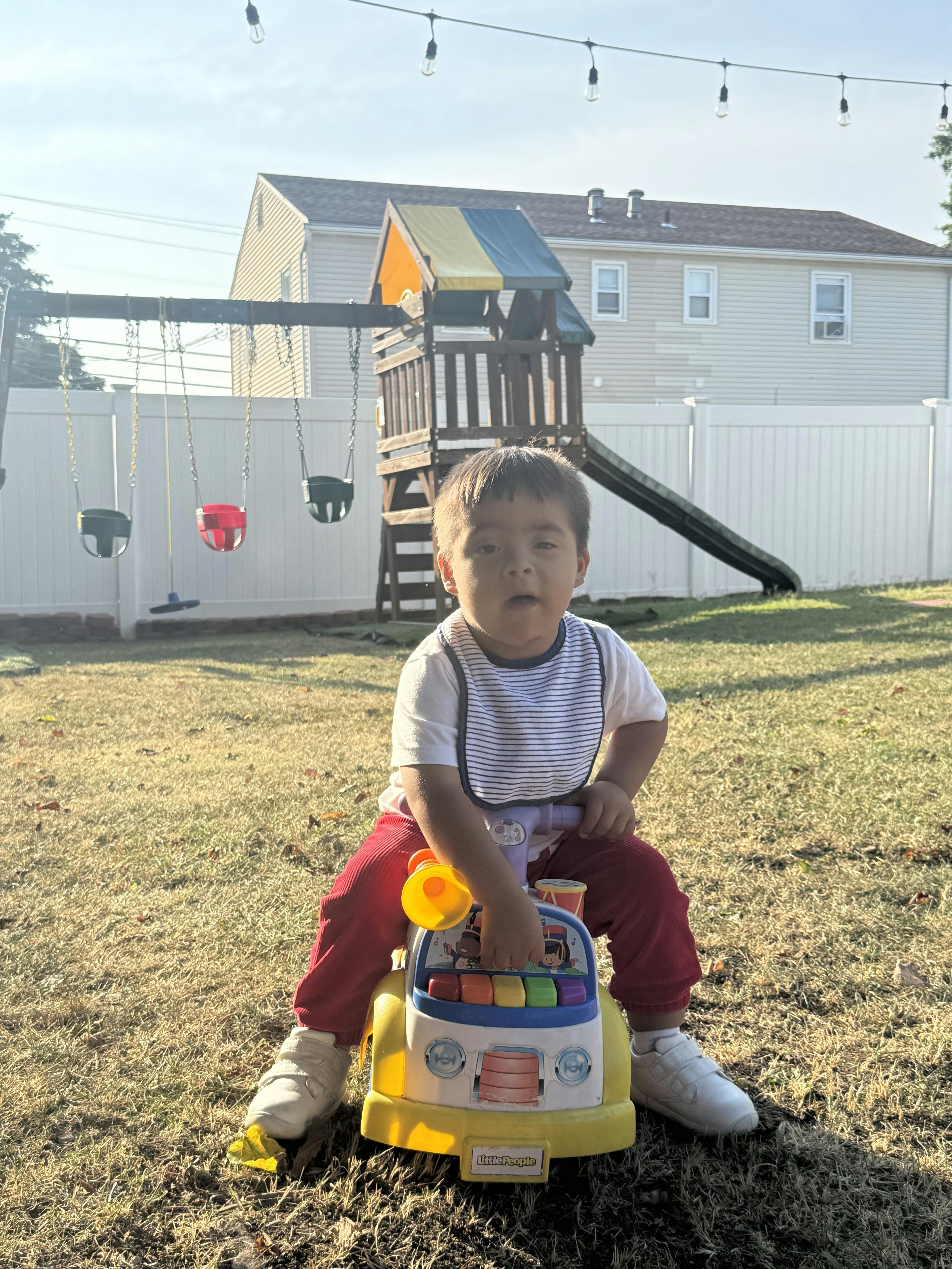 Child sitting on a toy car in a backyard
