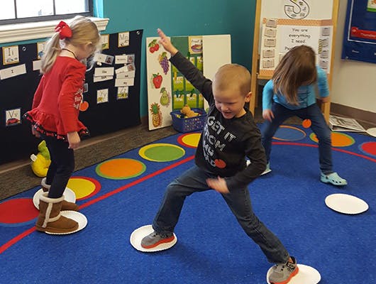 Three children playing a game on a colorful rug in a classroom
