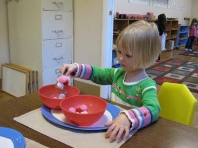 Child playing with pom-poms and bowls in a classroom