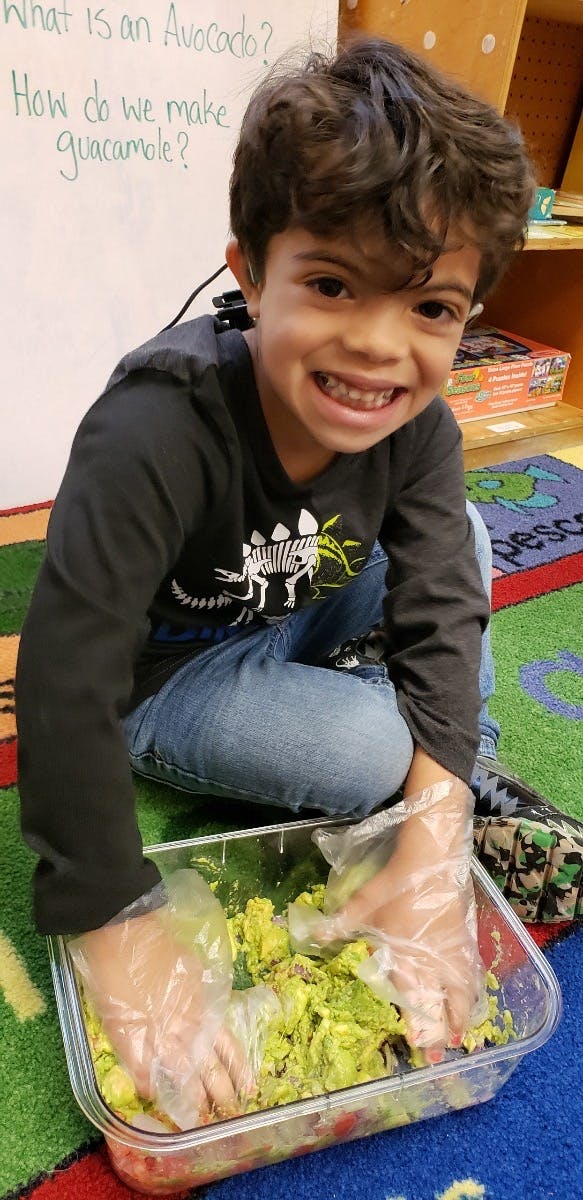 Child wearing gloves mixing guacamole in a clear container