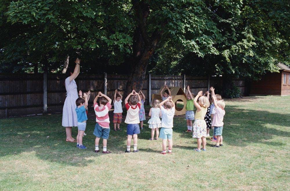 Adult and children standing in a circle with arms raised under a tree