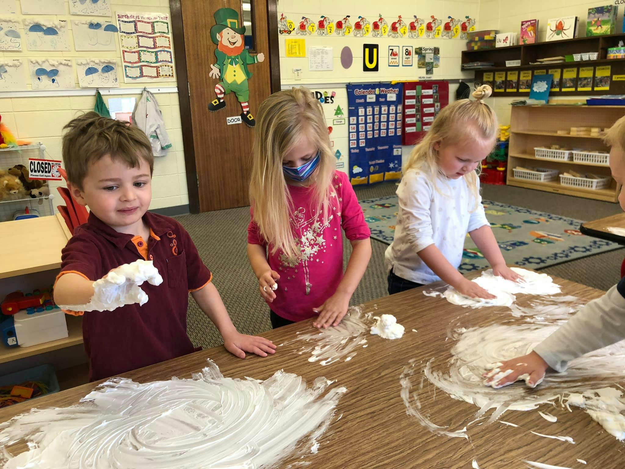 Children playing with shaving cream on a table in a classroom