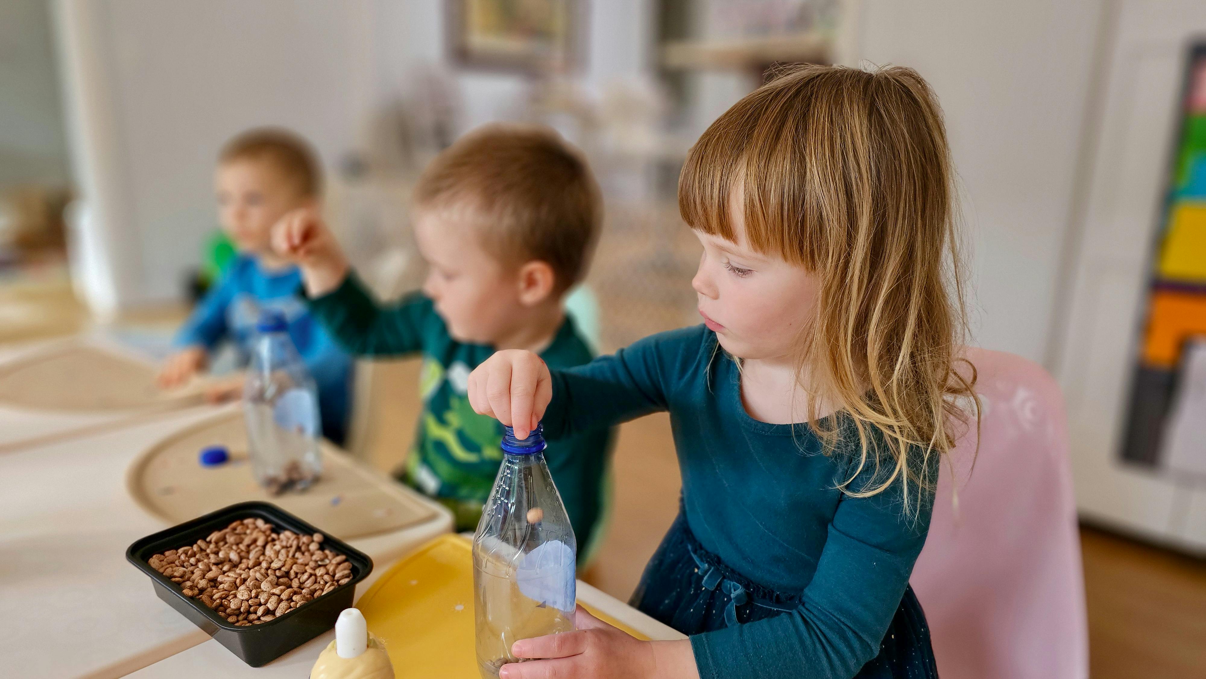 Child playing with a bottle and small objects at a table