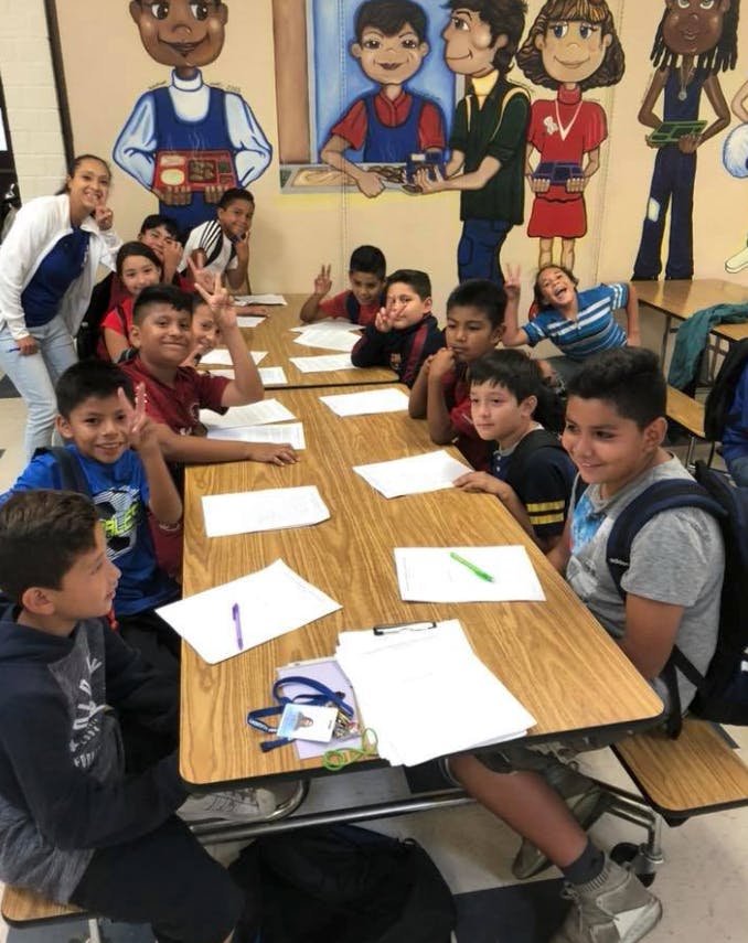 Group of children and one adult sitting at tables in a classroom