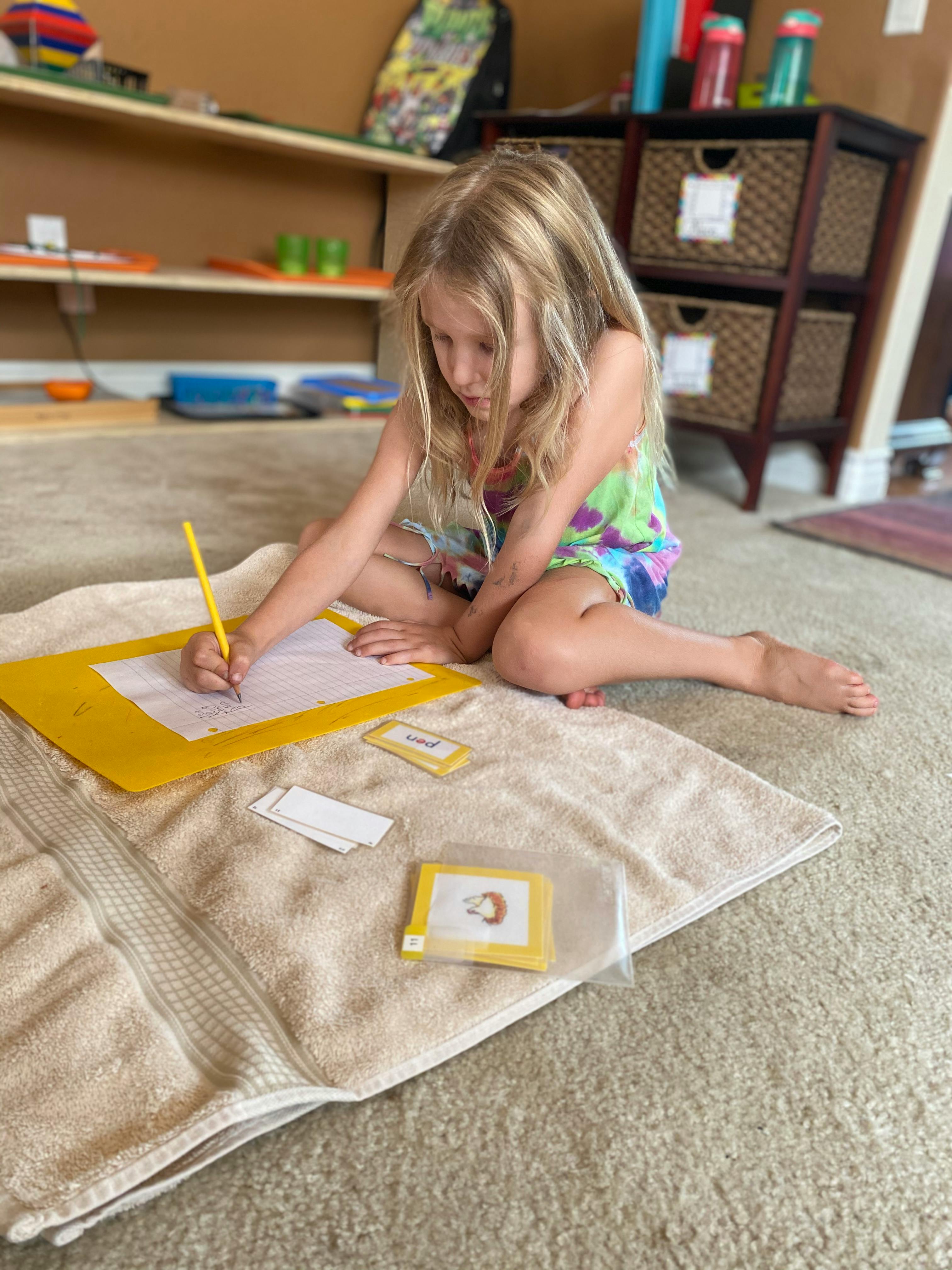 Child sitting on floor drawing on paper with a pencil