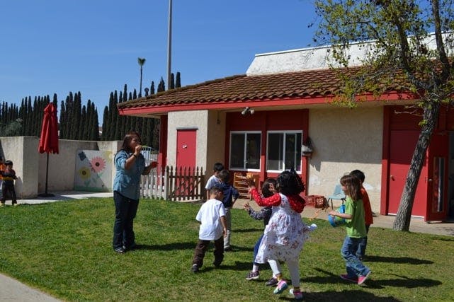 Adult and children playing outdoors on grass near a building