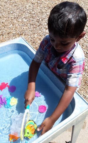 Child playing with toy fish in a water table