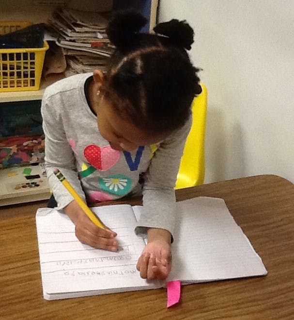 Child writing in a notebook with a pencil