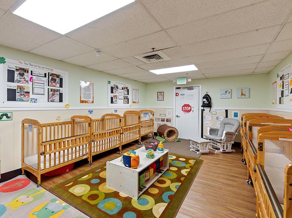 Cribs inside a nursery room with playmats and a rocking chair