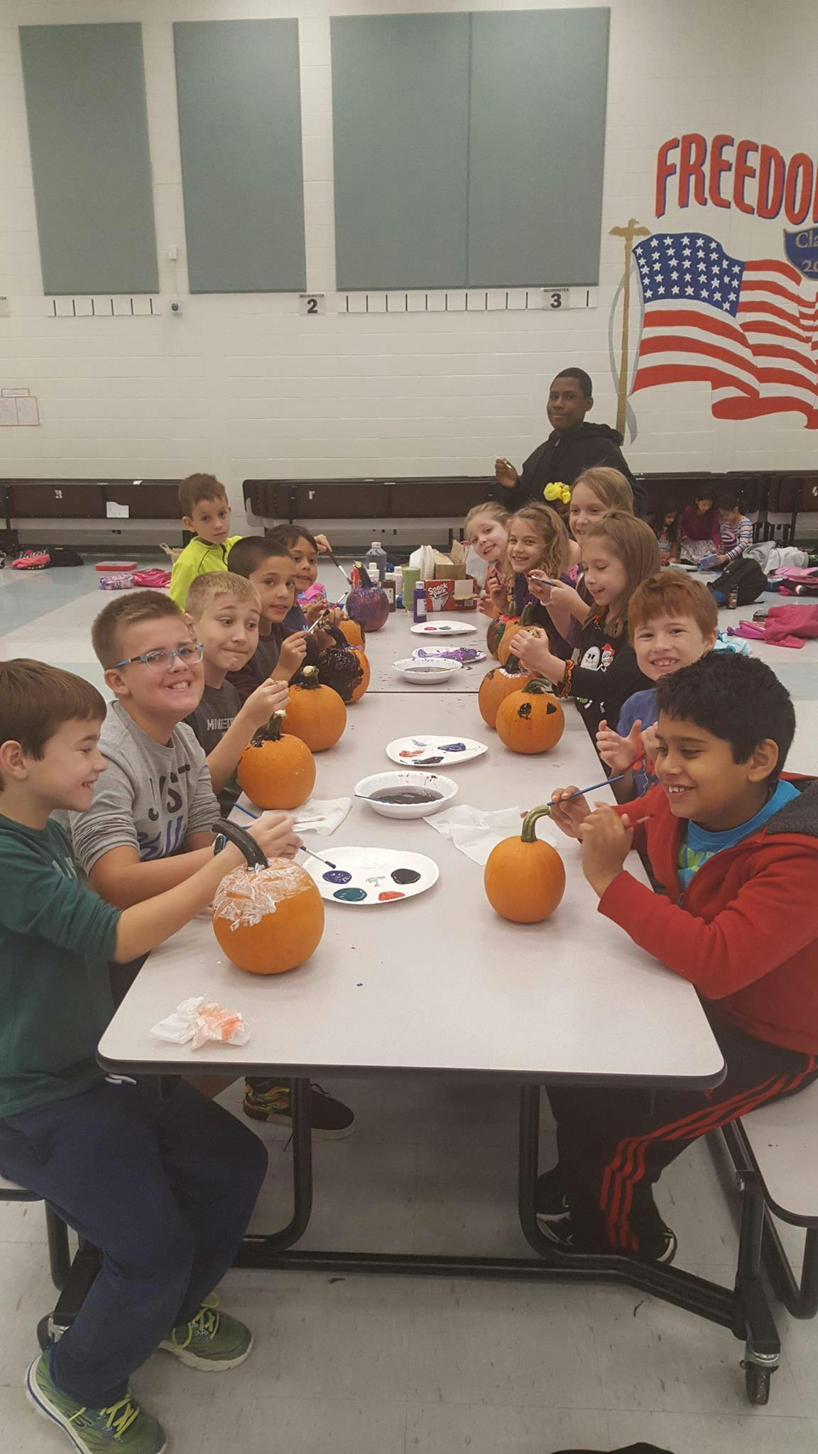 Children painting pumpkins at a long table