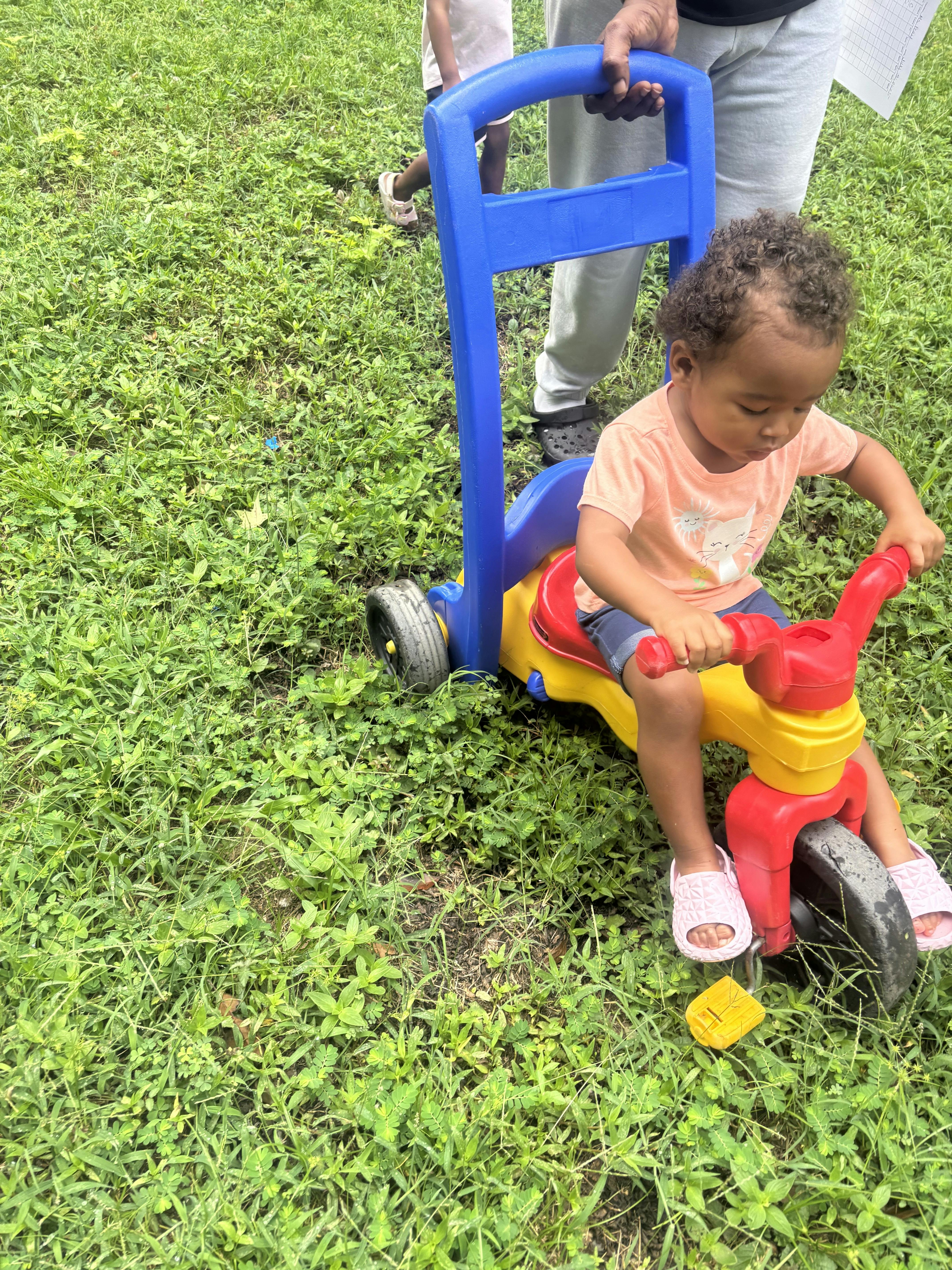 Child on a tricycle being pushed by a person
