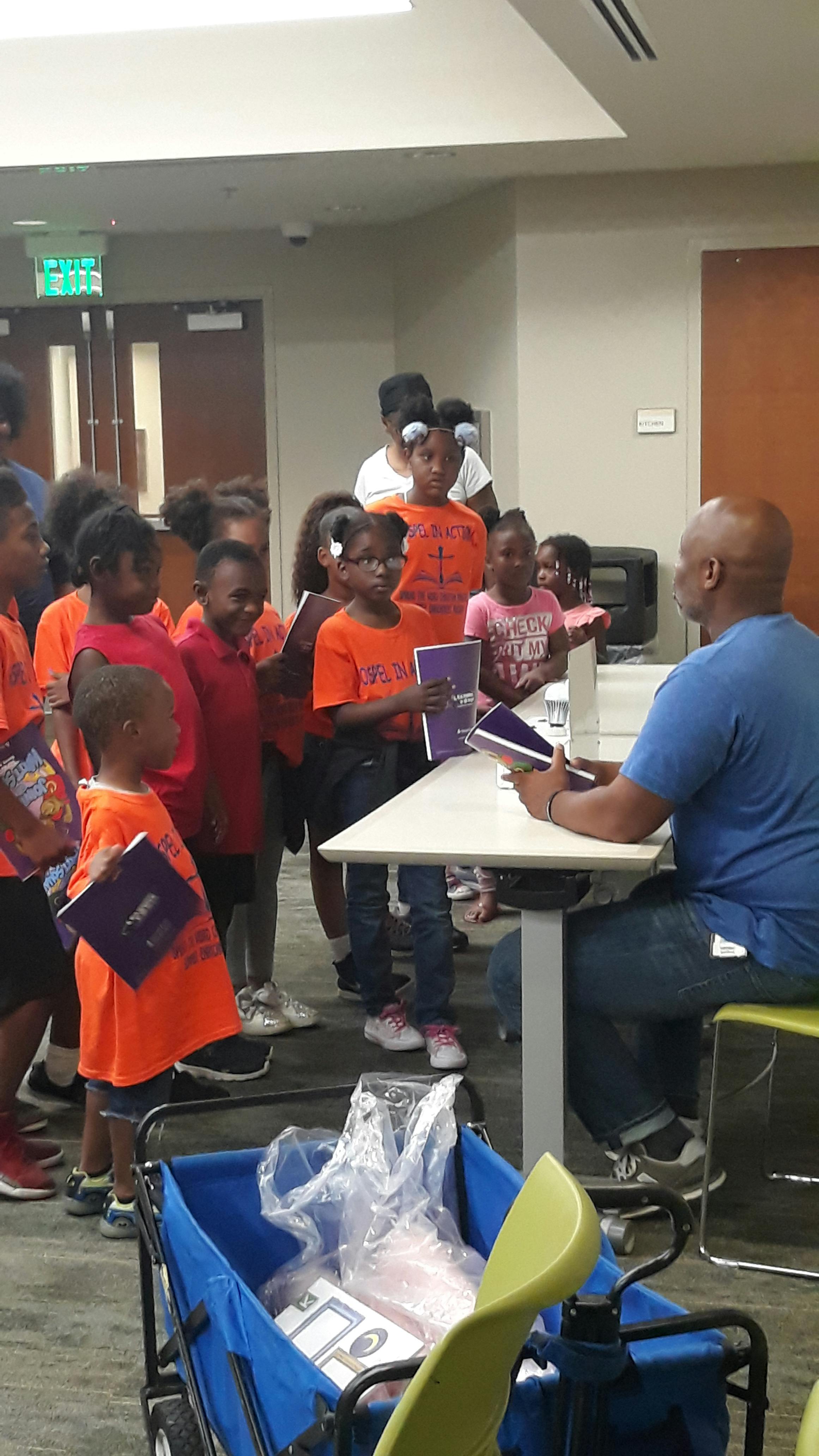 Adult sitting at table with children holding books standing around