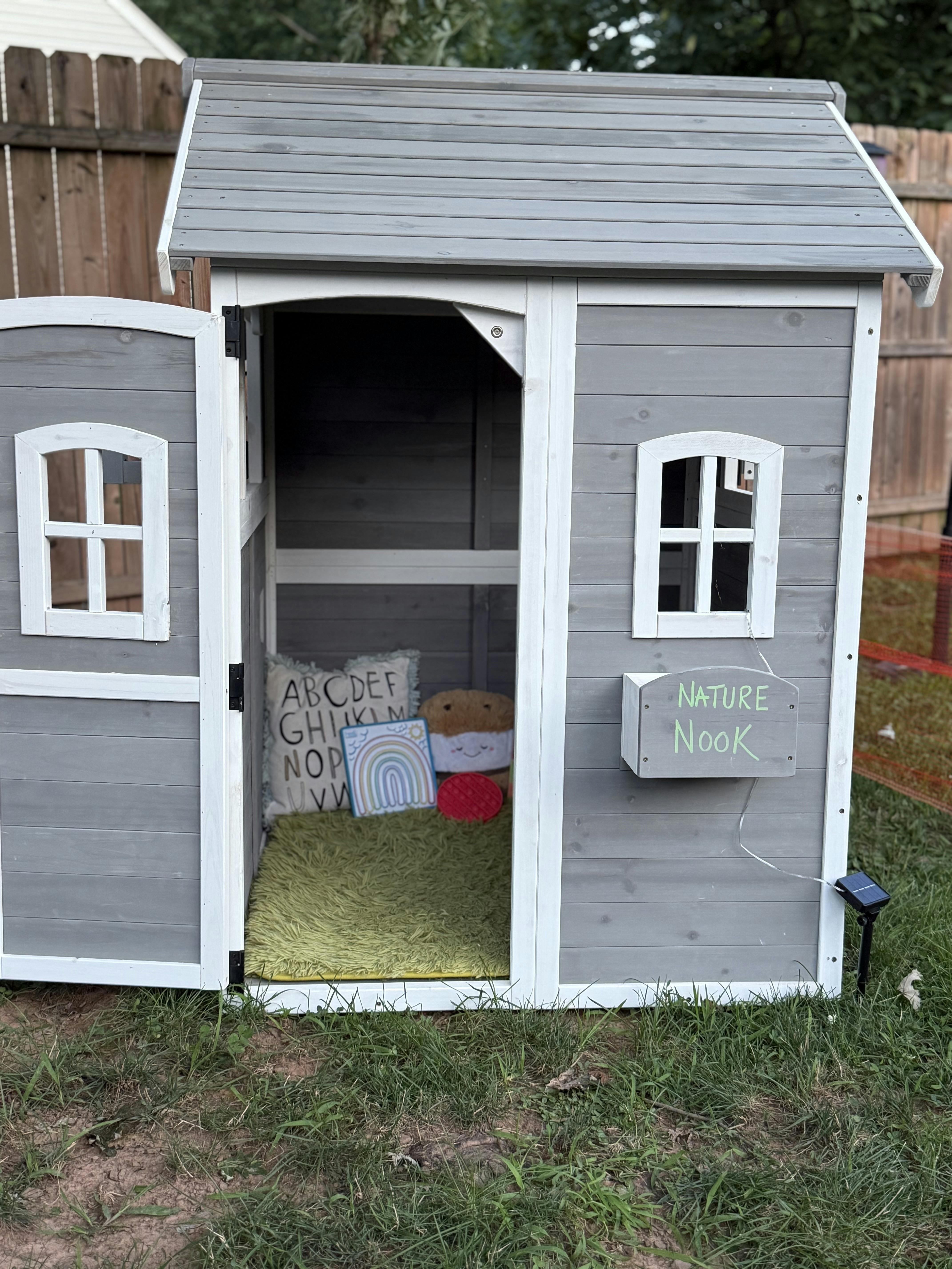 Wooden playhouse in a yard with a Nature Nook sign and interior decor