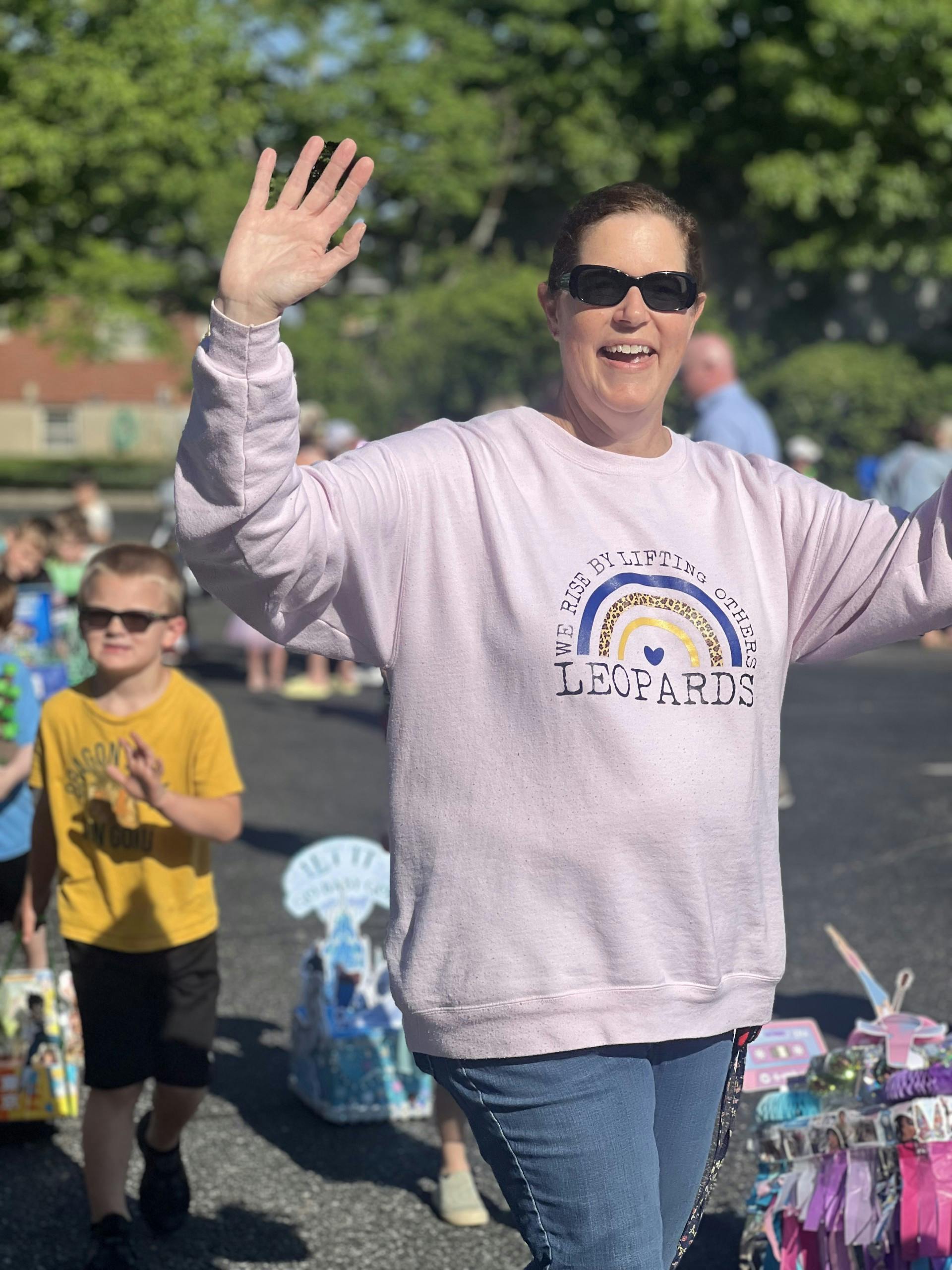 Person in sunglasses waving with a child in the background