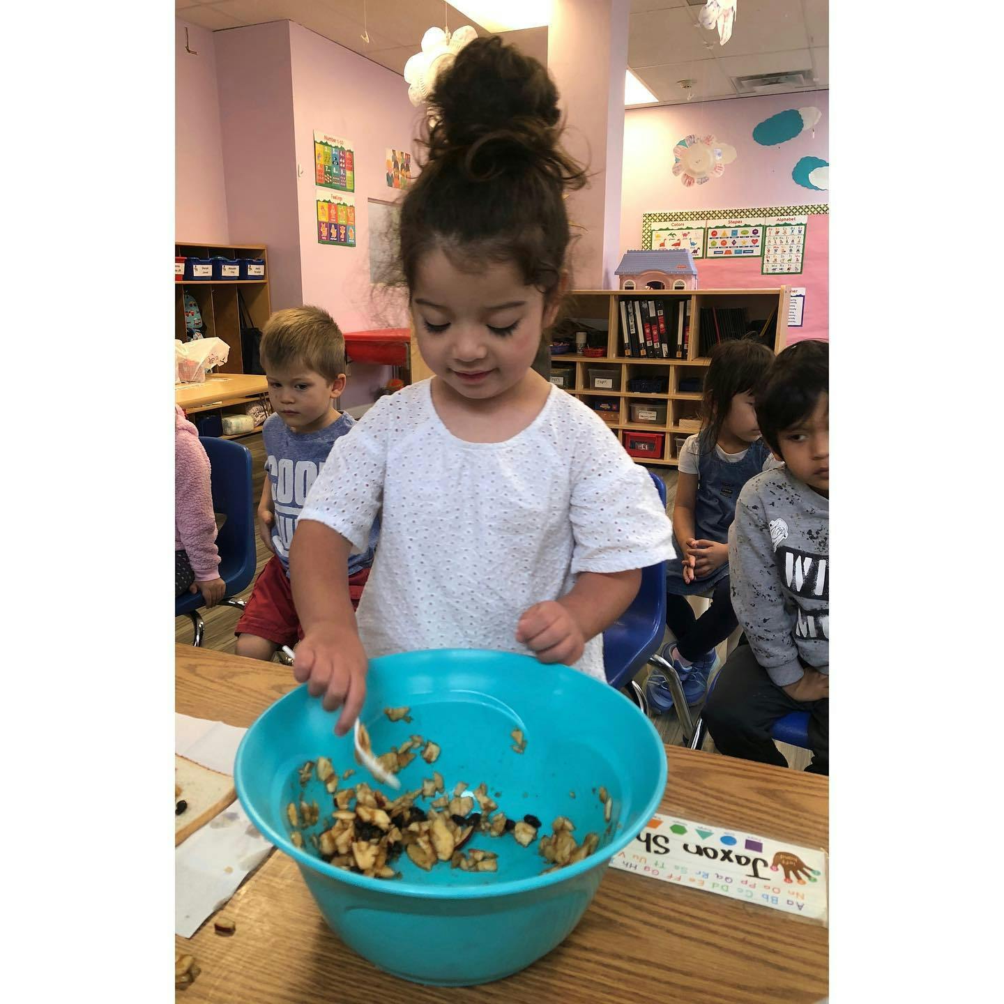 Child mixing ingredients in a large bowl in a classroom