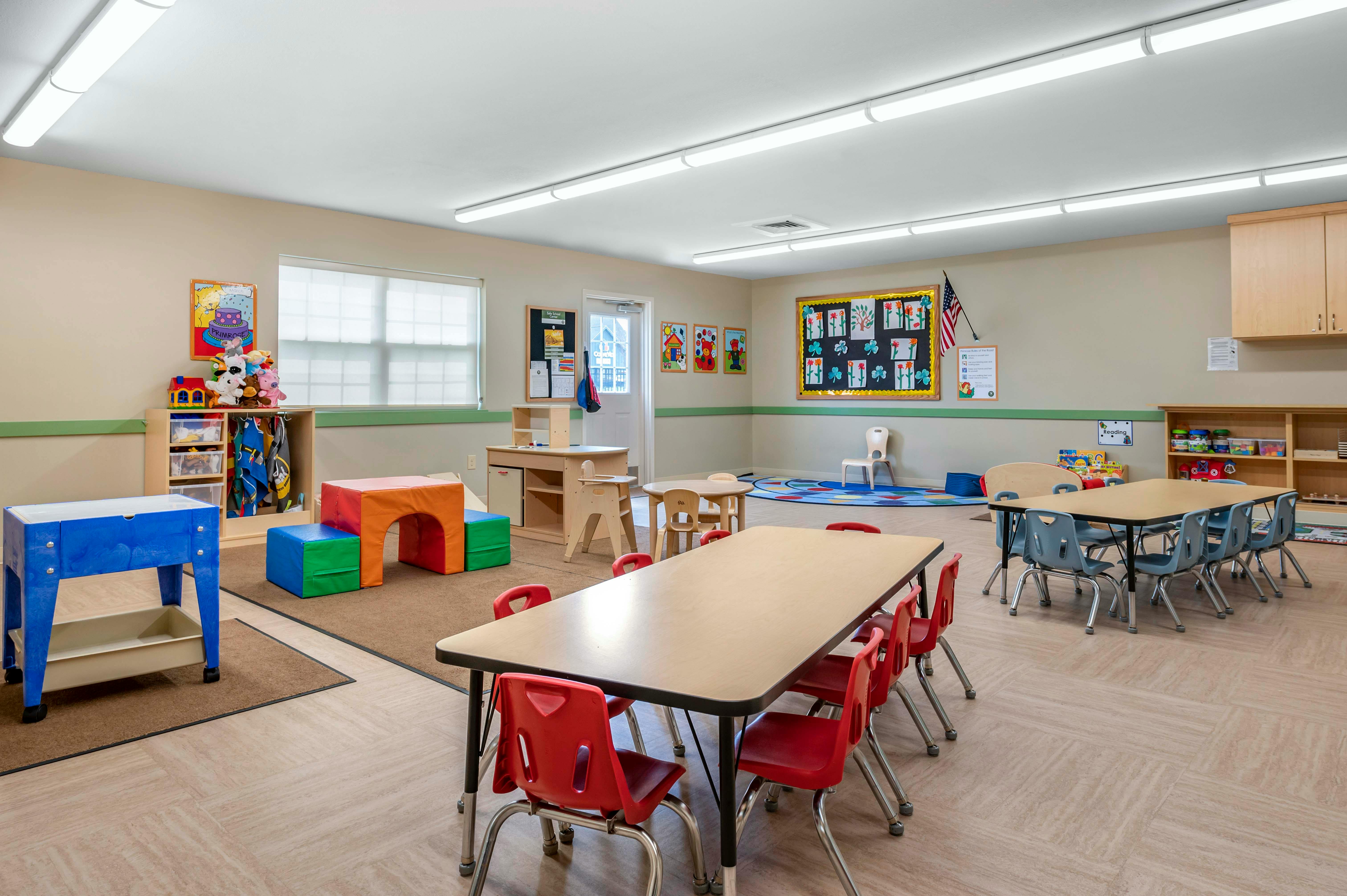 An empty classroom with several tables and chairs, play equipment, and decorations