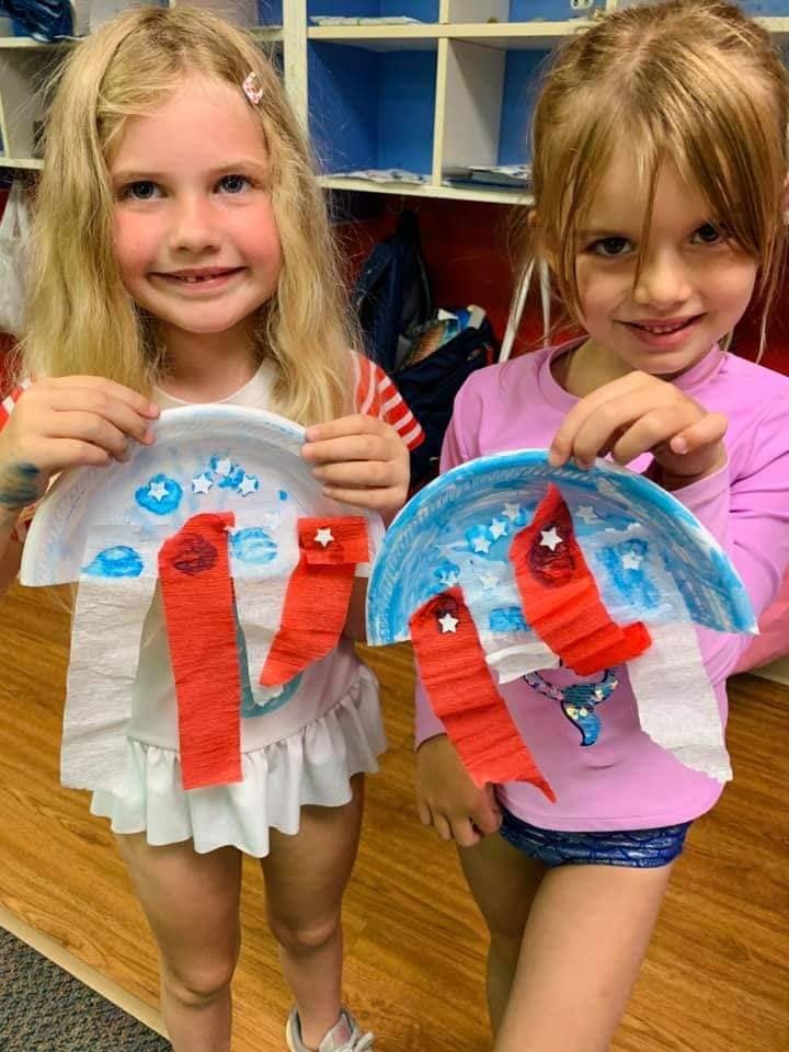 Two children holding up paper plate crafts with red and blue decorations