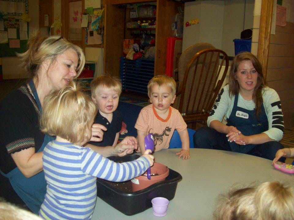 Two people and three children gathered around a table with a sensory bin