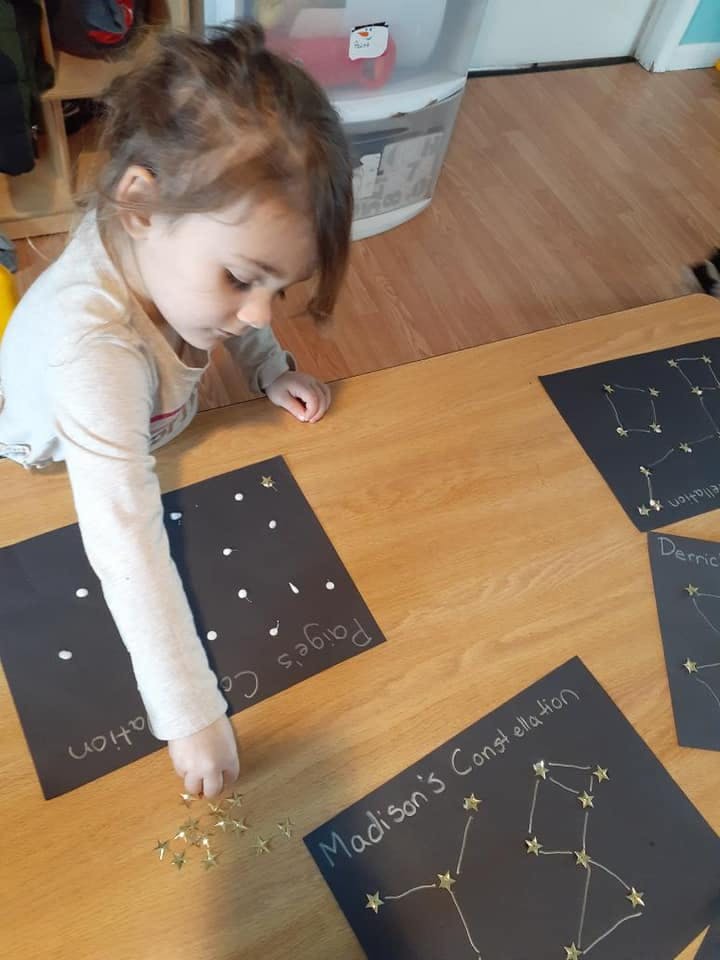 Child placing star stickers on a black paper with "Madison's Constellation" written on it"