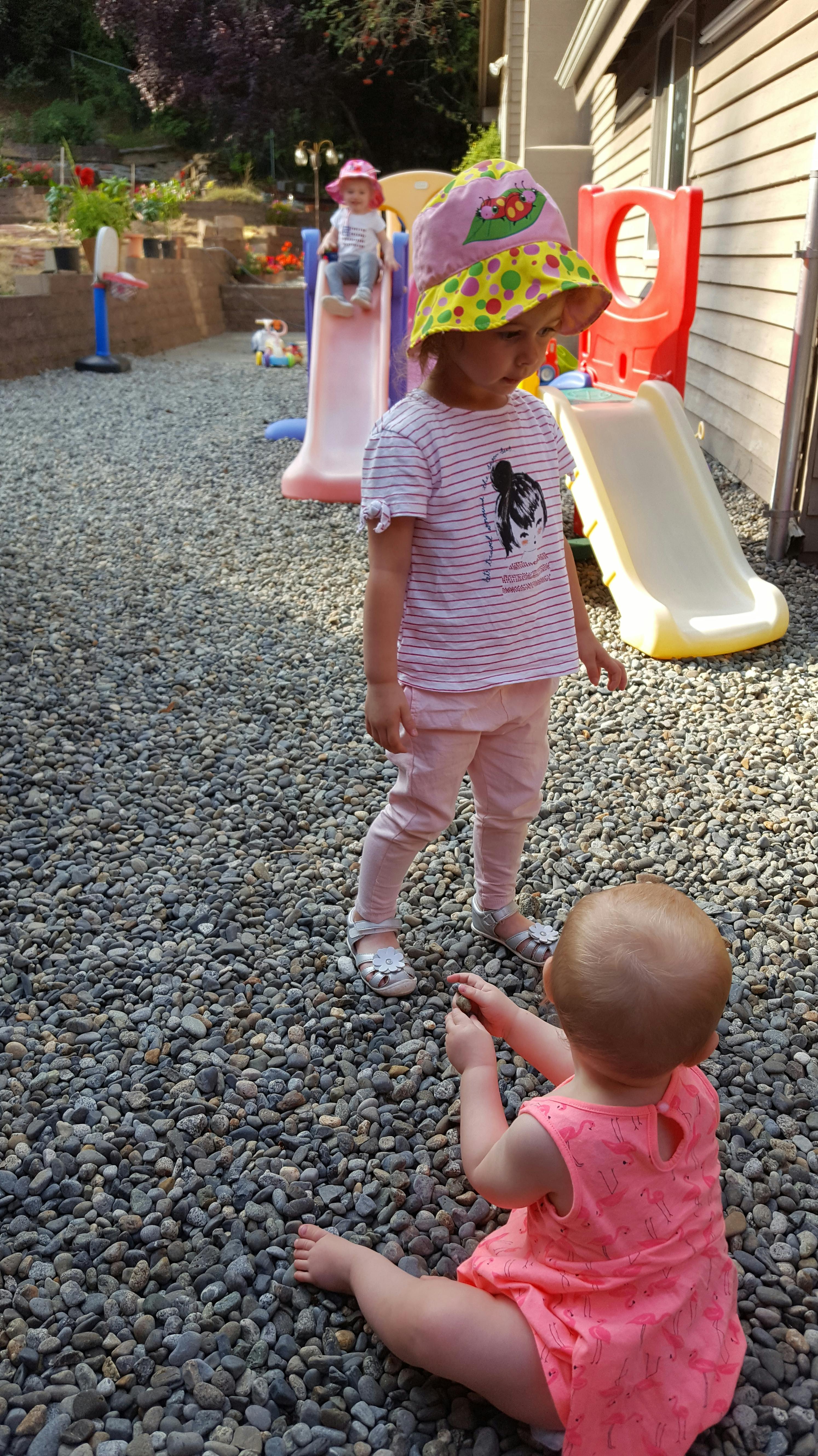 Two children playing on a gravel ground near toy slides
