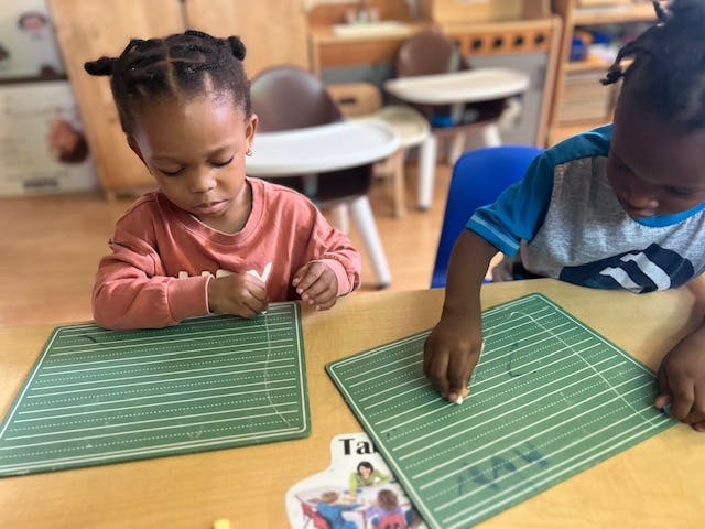 Two children writing on green boards at a table