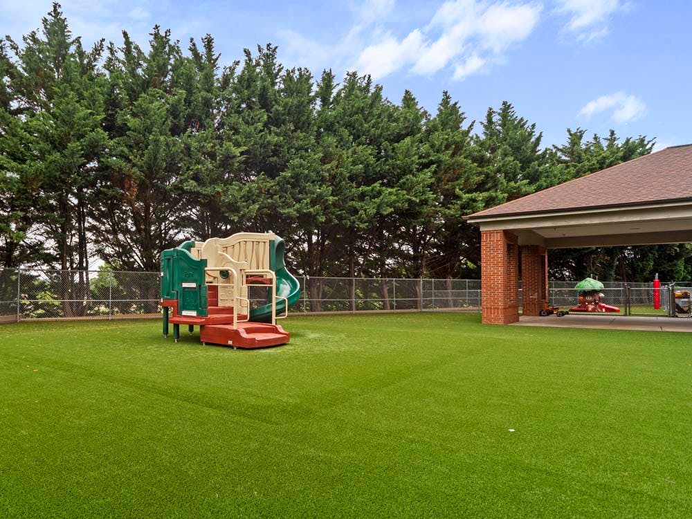 Playground with green turf, play structure, and covered brick area