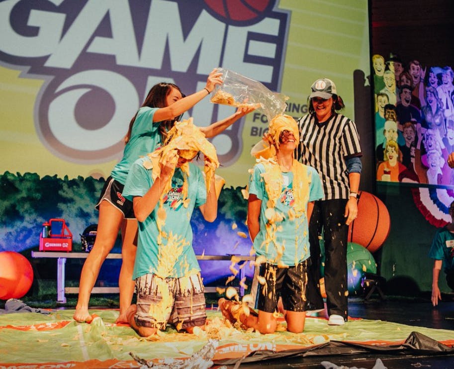 People on stage covered in yellow slime, one person pouring more
