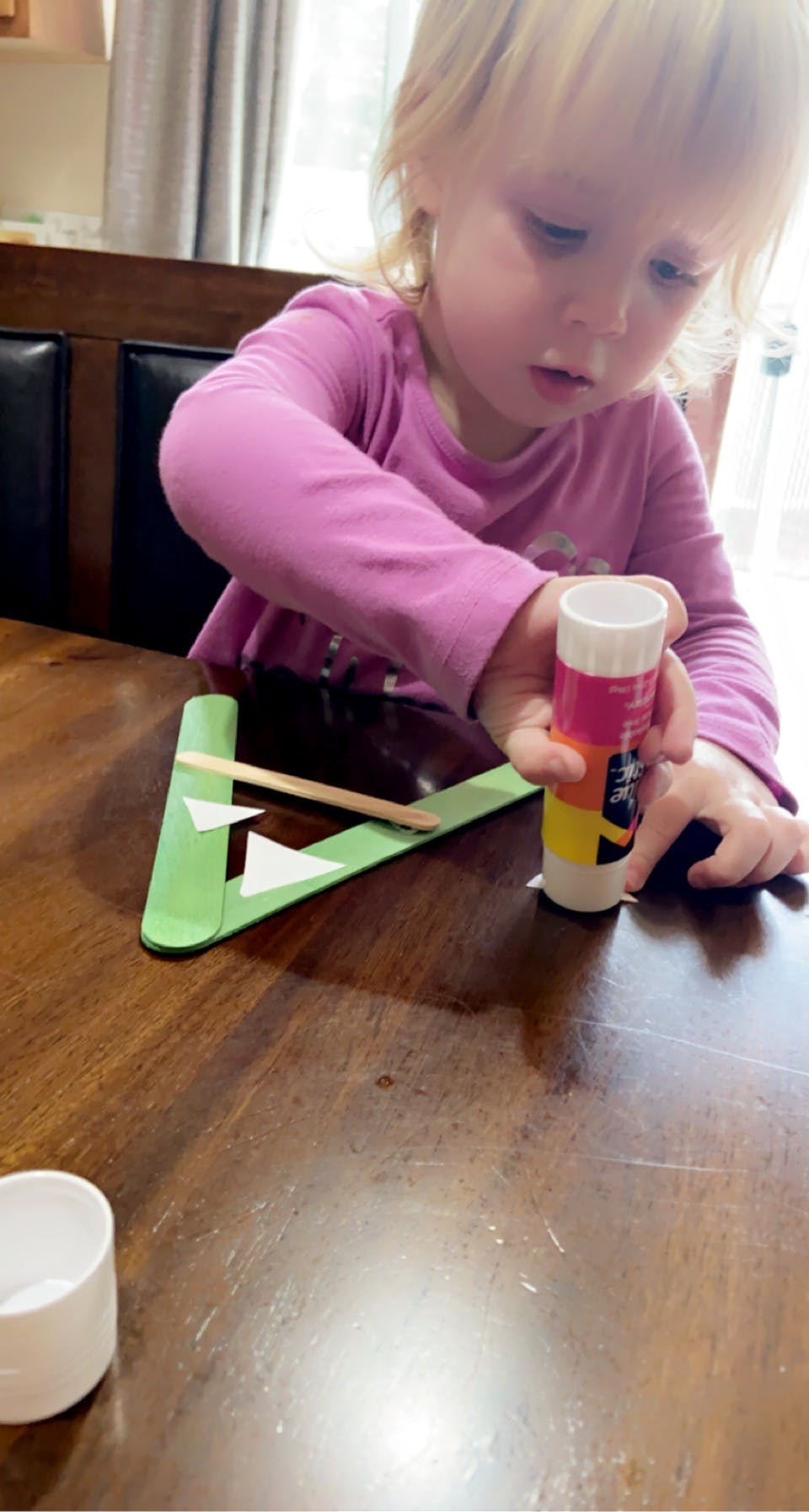 Child holding a glue stick over green paper craft
