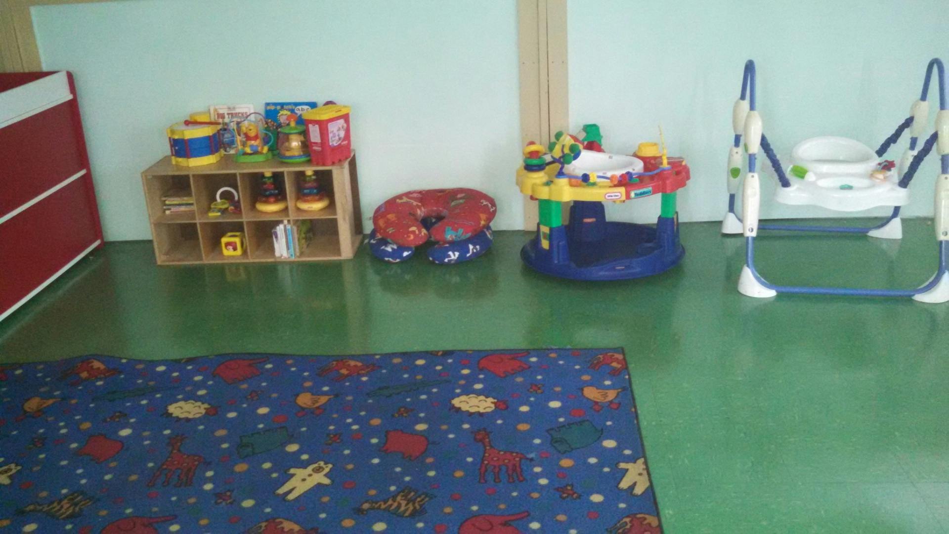 Playroom with a blue rug, toy shelf, baby bouncer, and activity center